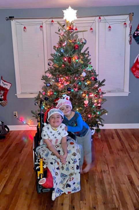 two children smiling in front of a christmas tree