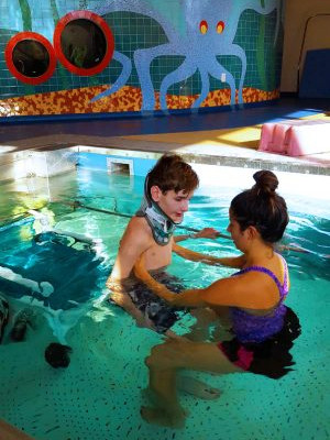 a boy in water therapy with a medical provider helping