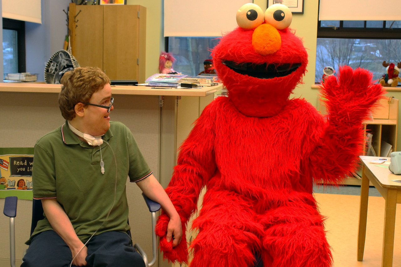 a boy holding the hand of a human sized elmo