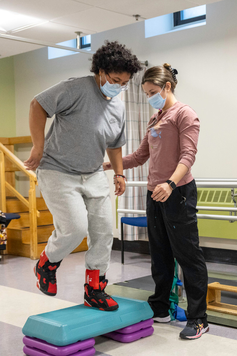 a girl stepping up during a PT session with a provider supporting her