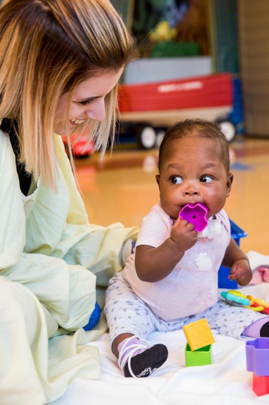 a young girl holding a toy to her mouth as a woman watches
