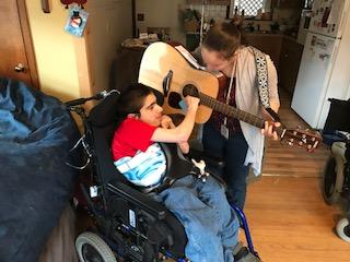 a boy in a wheelchair strumming a guitar with his teacher